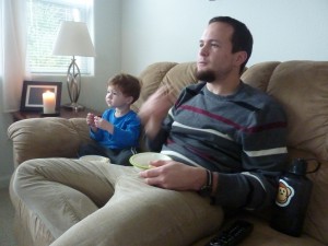 The boys eating popcorn and watching the big game.