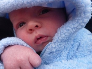 Simon is all bundled up to go outside and watch his big brother ride the tricycle